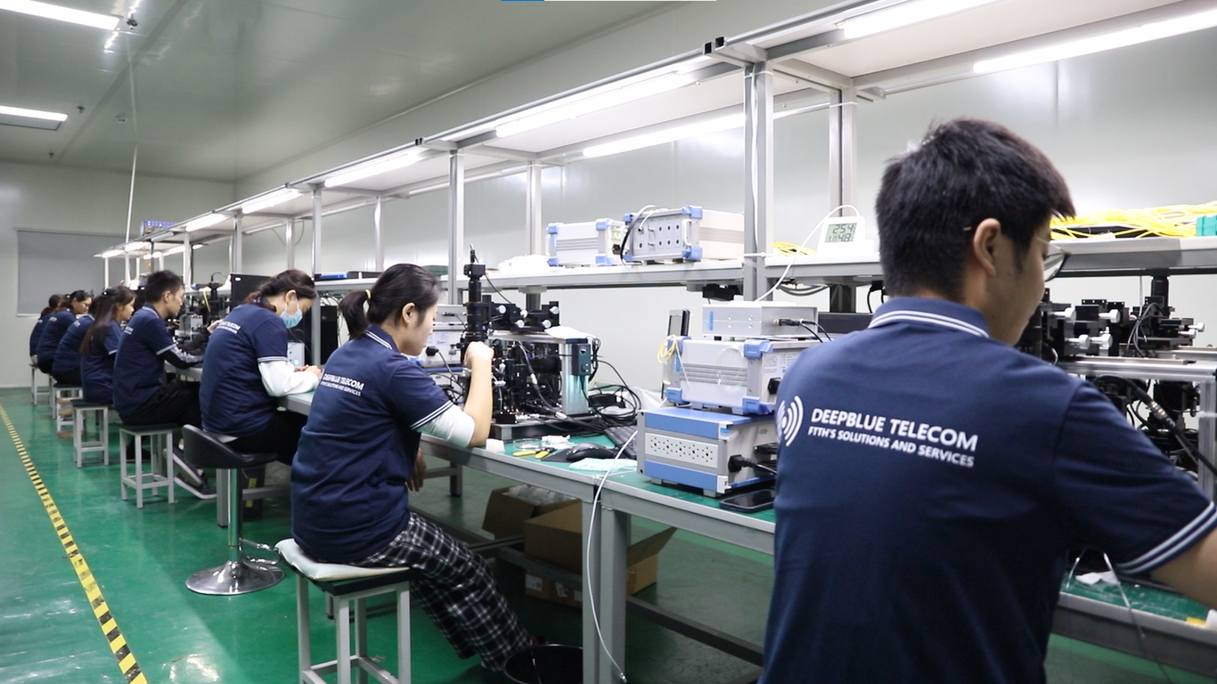 Technicians in blue uniforms assemble telecom equipment at a long production line in a clean factory.